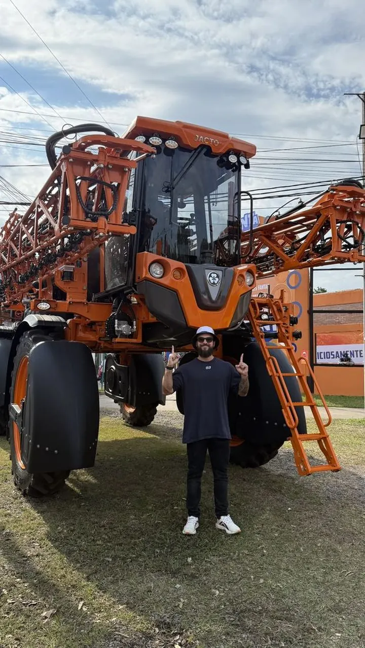Ele em pé em frente a uma grande máquina agrícola laranja