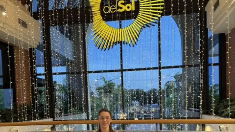 Pâmela sentada em um sofá curvo no saguão iluminado do Shopping Del Sol