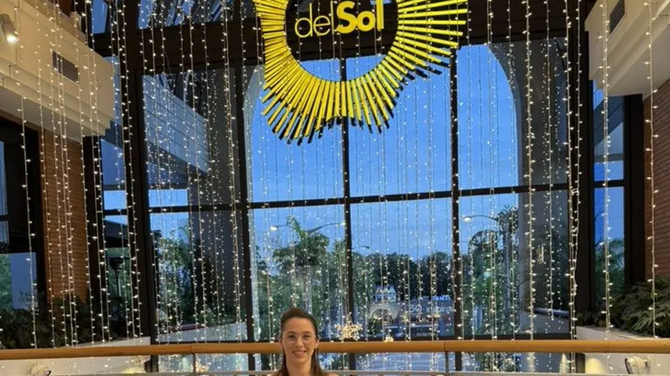 Pâmela sentada em um sofá curvo no saguão iluminado do Shopping Del Sol