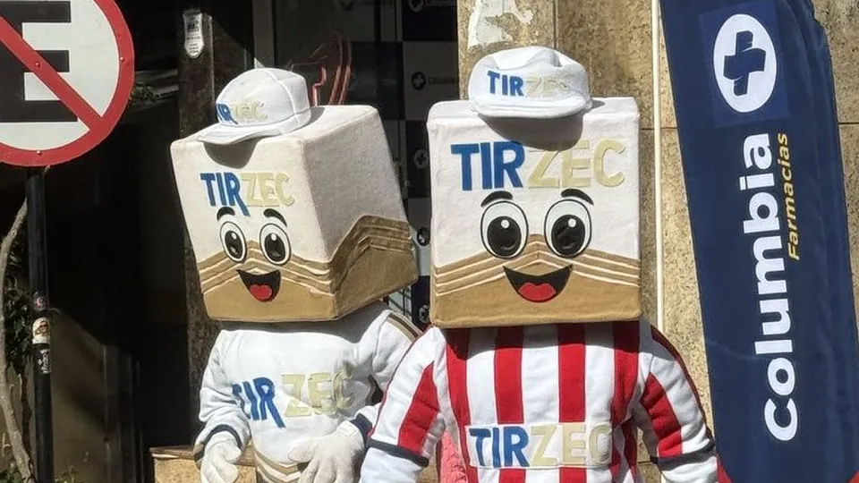 Dois mascotes fantasiados na calçada, um com camisa listrada vermelha e branca