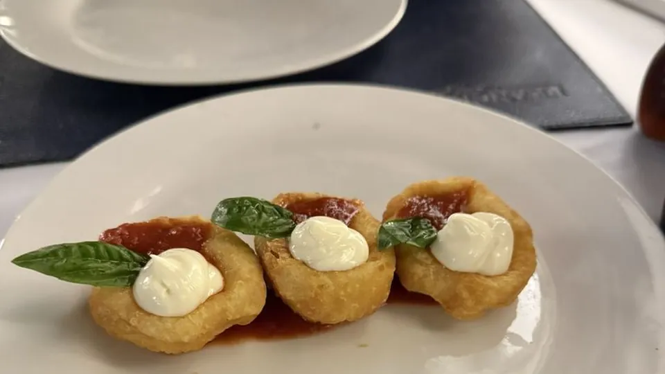 Prato com pequenos petiscos fritos cobertos com creme e manjericão