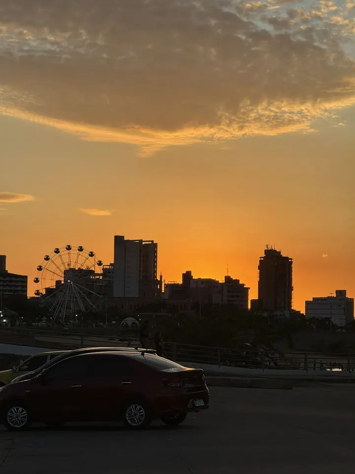 Pôr do sol alaranjado sobre a cidade, com uma roda-gigante na silhueta
