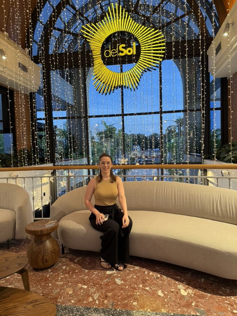 Pâmela sentada em um sofá curvo no saguão iluminado do Shopping Del Sol