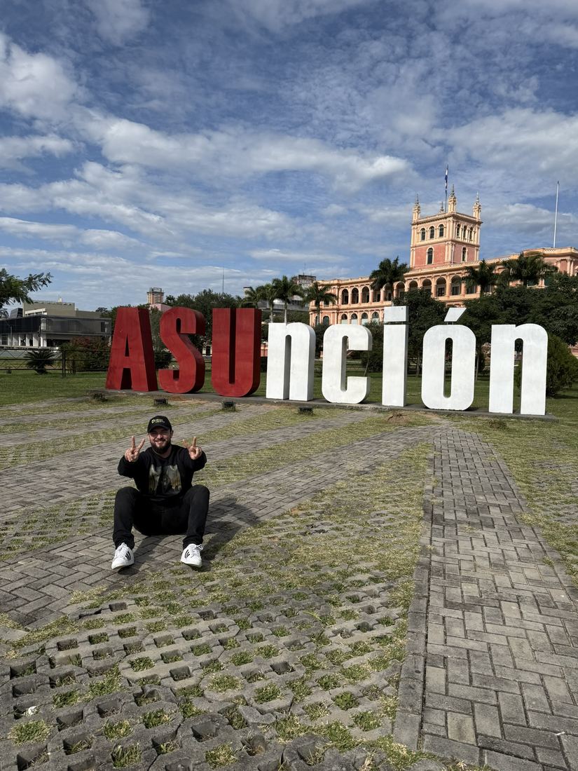 Ele agachado em frente ao letreiro colorido de Asunción