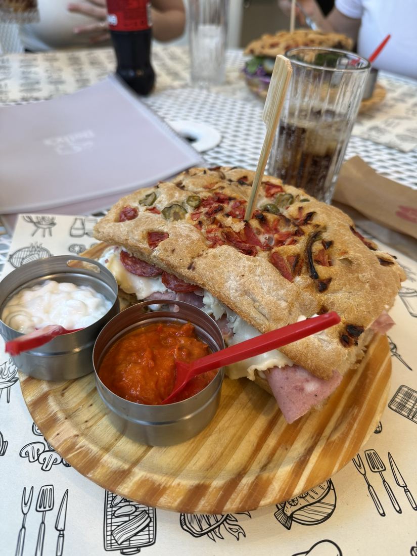 Sanduíche em tábua de madeira com molhos, em uma mesa de restaurante