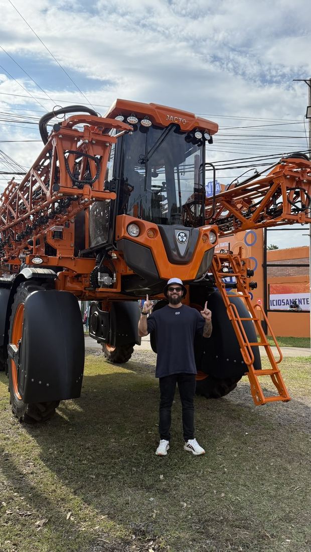Ele em pé em frente a uma grande máquina agrícola laranja