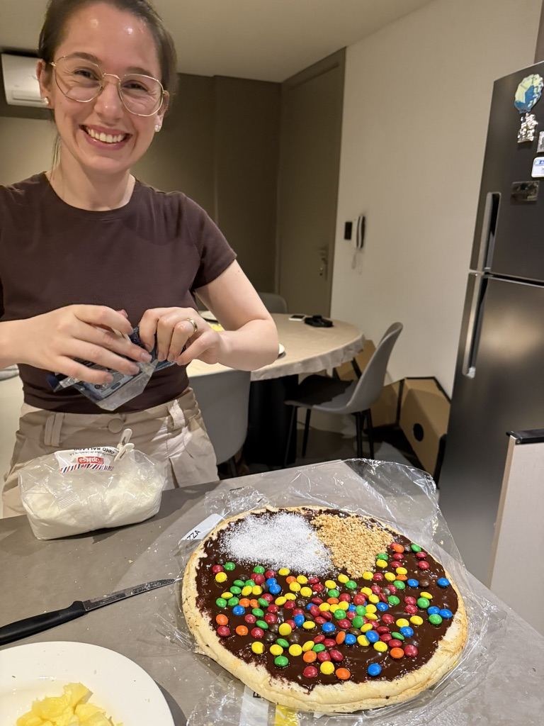 Ela sorrindo enquanto prepara uma pizza doce com confeitos coloridos